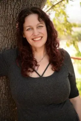 Katie Weatherup smiling with a tree in the background. She brings expertise to the question of What Is Soul Loss?