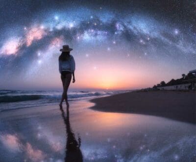 woman walking on beach under milky way