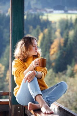 Girl with a cup of coffee sitting on the railing on the balcony. morning in a mountain hut for living soul purpose